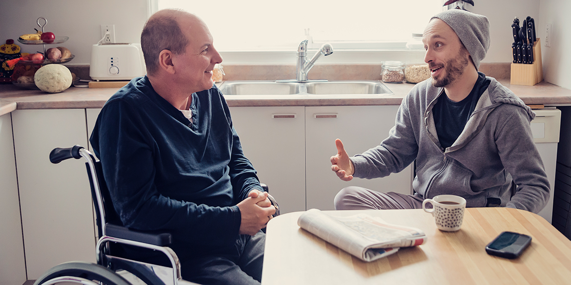 Homme en chaise roulante avec adulte en discussion dans cuisine